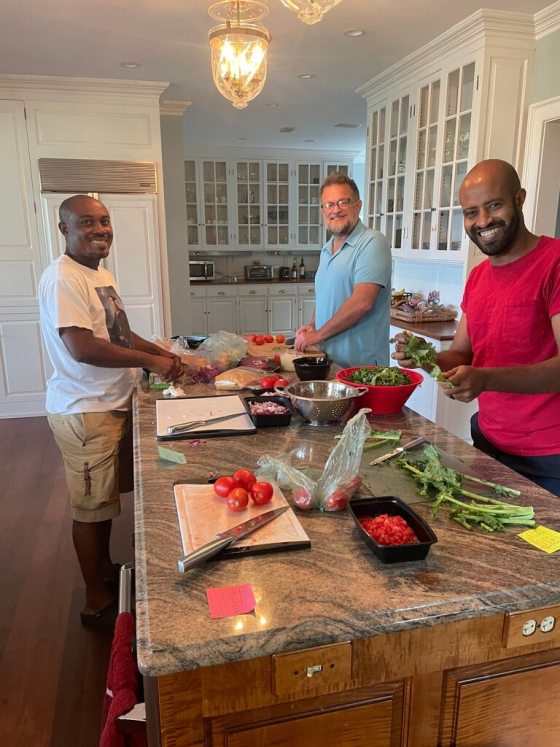 Three people standing around a kitchen island preparing food. 